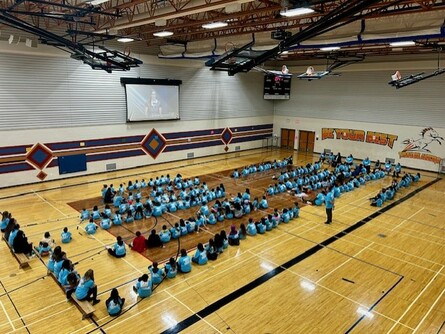 students sitting in the gym for an assembly wearing blue shirts